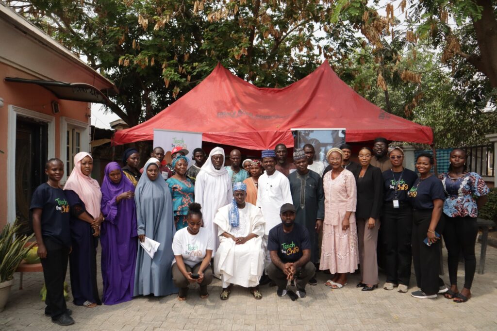 Men and women pose together for a photo in front of a red canopy